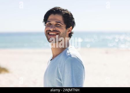 Ein junger, birassischer Mann lächelt hell am Strand Stockfoto
