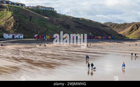 Ein Blick entlang des Strandes und der Promenade mit farbenfrohen Strandhütten in Saltburn by the Sea, England, UK. Leute laufen am Strand entlang. Stockfoto