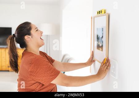 Eine junge Frau in Übergröße hängt zu Hause einen Bilderrahmen auf Stockfoto