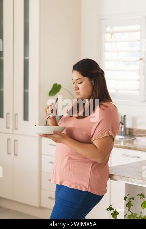 Eine junge Frau in Übergröße genießt eine Mahlzeit in einer modernen Küche Stockfoto