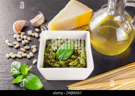 Hausgemachte Pesto-Sauce in einem kleinen weißen quadratischen Glas und Zutaten für Pasta auf schwarzem Steinhintergrund. Traditionelle italienische Küche, Rezept, Restaurant Me Stockfoto