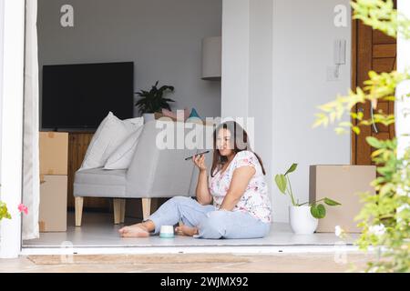 Eine junge Frau in Übergröße sitzt zu Hause, umgeben von Umzugskartons, mit unverändertem Kopierraum Stockfoto