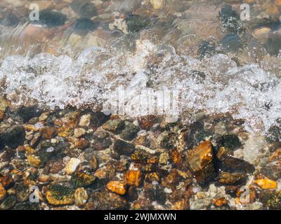 Wunderschöne Kieselsteine am Strand aus nächster Nähe. Wassersteine Küste felsig. Ein Nahblick auf einen Strand mit Felsen und Wasser. Die Welle Platzt Auf Dem Felsen. Stockfoto