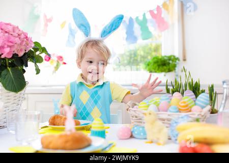 Osterfrühstück für die Familie. Kind mit Hasenohren am dekorierten Tisch mit Eierkorb, Küken und Kaninchen am Ostermorgen. Eierjagd und festliches Essen Stockfoto