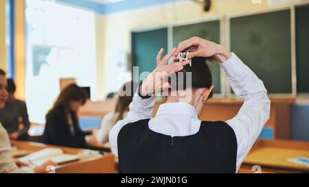 Ein Schulmädchen fixiert sich die Haare während des Unterrichts. Stockfoto