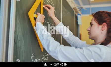 Ein rothaariges Schulmädchen zeichnet geometrische Formen auf die Tafel. Stockfoto