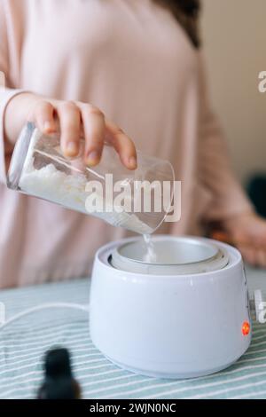 Vertikale Nahaufnahme einer nicht erkennbaren weiblichen Handwerkerin, die trockene Zutat aus dem Glasmessglas zur Herstellung einer Kerzenbildung gießt. Stockfoto