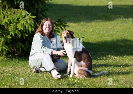 Eine Frau sitzt auf einer Wiese mit einem großen Hund im Sommer Russland Jaroslawl 10. August 2023 Stockfoto