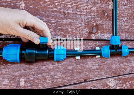 Nahaufnahme der Hand, die die Wasserversorgung einer Kunststoffwasserversorgung im Freien durch Drehen des Hebels am Kugelhahn absperrt. Stockfoto