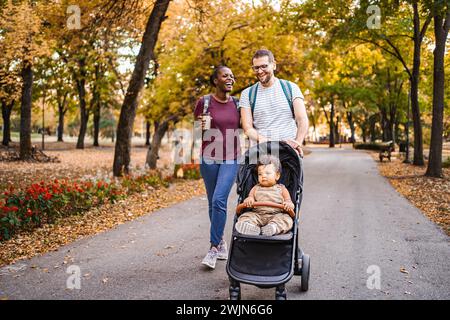 Gemischte Rassen-Paare gehen mit dem Kinderwagen ihres Sohnes durch den Park Stockfoto