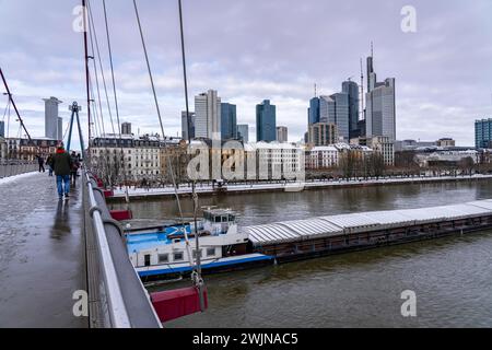 Winter in Frankfurt, Blick auf die Skyline des Stadtzentrums, von der Fußgängerbrücke Holbeinsteg, Frachter auf dem schneebedeckten Main, Stockfoto