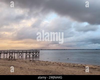 Leerer hölzerner Pier zur Ria de Aveiro in Portugal mit dramatischem Himmel und ruhigem Wasser. Torreira, Murtosa - Portugal. Stockfoto