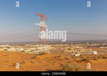 Wüstenlandschaft mit Al Digdaga Dorf in Ras al Khaimah, VAE, goldene Wüstendünen mit Hochspannungsturm und Wohngebäuden. Stockfoto