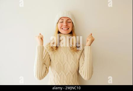 Überfröhliche glückliche Frau, die Siegergeste feiert, geballte Fäuste sagt ja und drückt Emotionen der Freude und des Sieges in Strickpullover und Hut aus Stockfoto