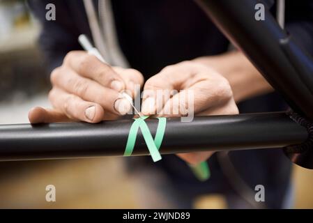 Nicht erkennbare Person, die einen Fahrradrahmen mit einem Skalpell und Abdeckband für eine individuelle Bemalung in seiner Fahrradwerkstatt vorbereitet. Stockfoto