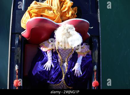Venedig, VE, Italien - 13. Februar 2024: Elegante Frau in Maske mit großer Perücke während der Gondelfahrt während des venezianischen Karnevals Stockfoto