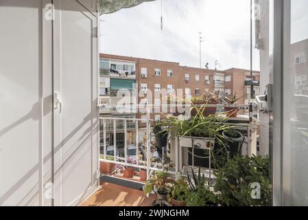 Eine kleine Terrasse mit einem weißen Aluminiumschrank, Metallgeländer und einigen geschäftigen Plattformen mit Blick auf eine städtische Straße mit Wohngebäuden Stockfoto