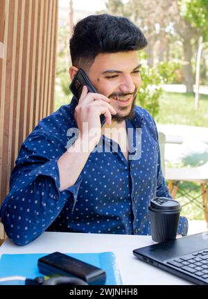 Gutaussehender Geschäftsmann, der am Laptop arbeitet und telefoniert. Stockfoto