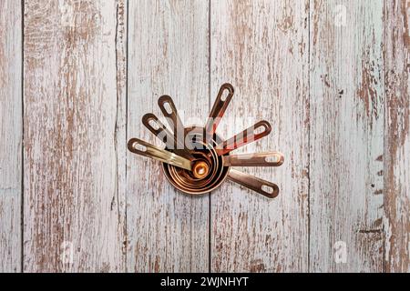 Stillleben mit Messbecher aus Kupfer unterschiedlicher Größe auf einer Holzoberfläche Stockfoto