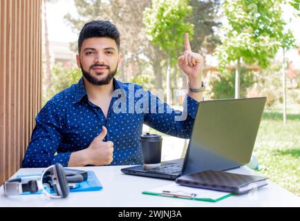 Junger Unternehmer, der am Tisch sitzt und draußen arbeitet. Stockfoto