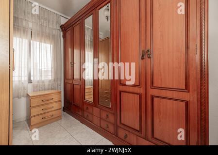 Kleines Schlafzimmer mit großen Schränken, die alles mit sapelfarbenem Holz und Spiegeln an den Mitteltüren füllen Stockfoto
