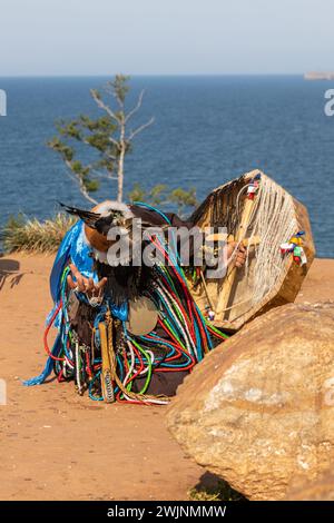 Ein Schamane in bunten Gewändern und Trommeln führt ein Trance-Ritual auf dem heiligen Schamanenfelsen von Olkhon am Baikalsee durch. Stockfoto