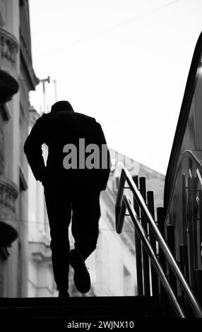 Verschwommene Silhouette eines jungen Mannes mit Händen in Taschen, der allein die U-Bahn-Treppe der Stadt mit glänzenden Geländern hinaufgeht Stockfoto