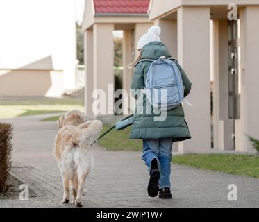 Mädchen Mit Golden Retriever Schlendert Im Frühjahr Die Straße Hinunter, Von Hinten Gesehen Stockfoto