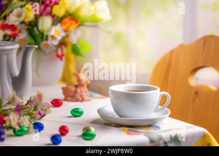 Eine Kaffeetasse auf einem Tisch mit Osterdekoration und einem bunten Blumenstrauß im Hintergrund Stockfoto