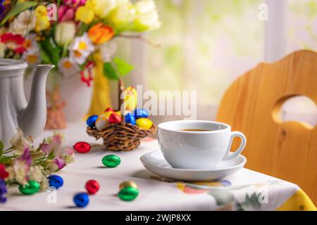 Eine Kaffeetasse auf einem Tisch mit Osterdekoration und einem bunten Blumenstrauß im Hintergrund Stockfoto