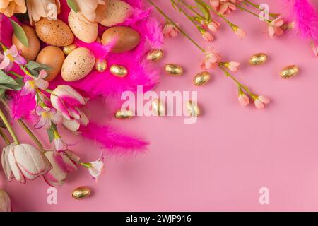 Arrangement in Rosa und Gold aus Blumen, Federn und Ostereiern auf rosa Hintergrund Stockfoto