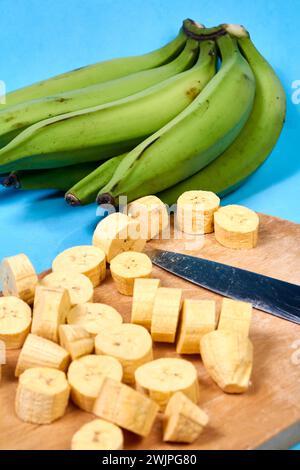 Frische grüne Banane auf blauem Hintergrund, Maqueno, Barraganete, Dominico. Hände Tischmesser Stockfoto