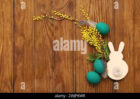 Osterkomposition mit bemalten Eiern, Mimosa und Hasenfigur auf Holztisch Stockfoto