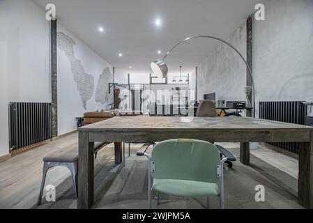 Großes Wohnzimmer in einem Loft-Haus, ungeschminkter Holztisch, offene Küche mit grauen Möbeln, hellen Holzfußböden und Möbeln im industriellen Stil Stockfoto