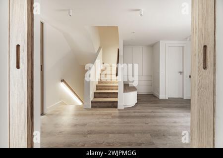 Eingangshalle eines Einfamilienhauses mit einem Holzsitz mit großen Schubladen darunter neben Treppen mit Holztreppen und Handläufen mit LED-Lichtleiste Stockfoto