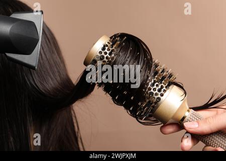 Friseur föhnt das Haar des Kunden auf hellbraunem Hintergrund, Großaufnahme Stockfoto
