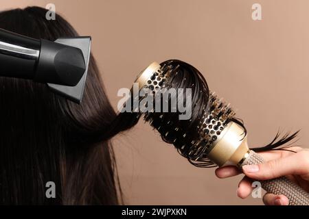 Friseur föhnt das Haar des Kunden auf hellbraunem Hintergrund, Großaufnahme Stockfoto