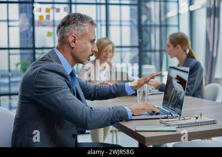 Selbstbewusster Geschäftsmann, der am Konferenztisch in einem modernen Büro sitzt Stockfoto