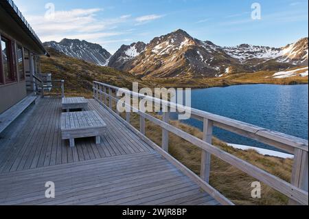 Holzhütte am See: Rustikale Hütte, eingebettet am Wasser mit schneebedeckten Bergen Stockfoto
