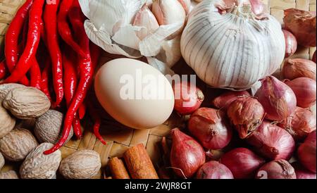 Foto von Gewürzen in Form von Schalotten, Knoblauch, Chilis und Eiern, die in einem gewebten Bambus angeordnet sind Stockfoto