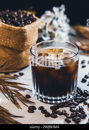 Eiskaffee schwarz im Glas und Kaffeebohnen. Kaltes Sommergetränk auf Holztisch mit Kopierraum. Eiskaffee Americano. Stockfoto