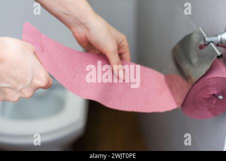 Eine weibliche Hand, eine Frau mit einer Rolle rosa Toilettenpapier, Verdauungsprobleme und Defäkationsstörungen. Stockfoto