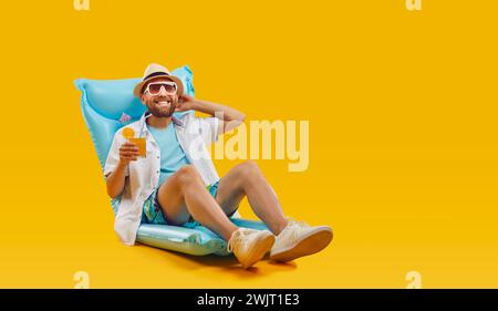 Glücklicher Mann, der sich auf aufblasbarer Matratze mit Cocktail über orangefarbenem Hintergrund entspannt Stockfoto