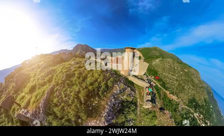 Aus der Vogelperspektive einer Frau, die auf der Stadtmauer von Borsh Castle in Albanien steht und über das Ionische Meer blickt. Sie lächelt und nimmt die Aussicht ein. Stockfoto