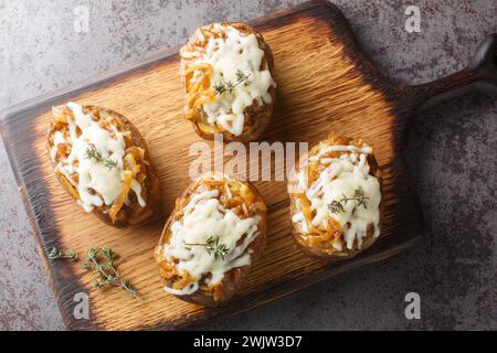 Die Kartoffeln mit französischen Zwiebeln sind von der klassischen Suppe inspiriert und werden mit karamelisierten Zwiebeln und Käse aus der Nähe auf dem Holzbrett auf dem Tisch garniert. Stockfoto