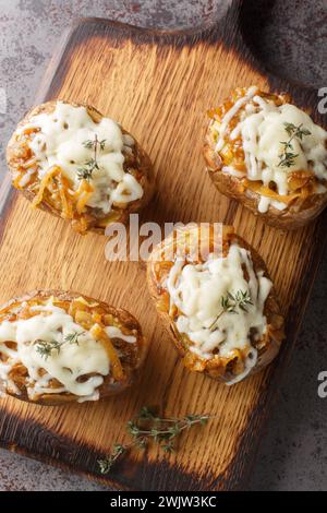 Käsige französische Zwiebeln gebackene Kartoffeln aus der Nähe auf dem Holzbrett auf dem Tisch. Vertikale Draufsicht von oben Stockfoto