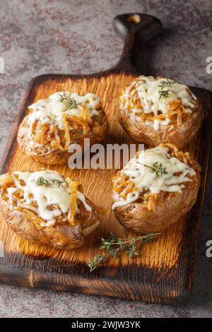 Käsige französische Zwiebeln gebackene Kartoffeln aus der Nähe auf dem Holzbrett auf dem Tisch. Vertikal Stockfoto