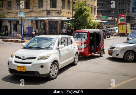 Moderne Autos und ein Bajaji oder Tuk Tuk fahren in einer Straße im Zentrum von dar es Salaam, Tansania. Stockfoto