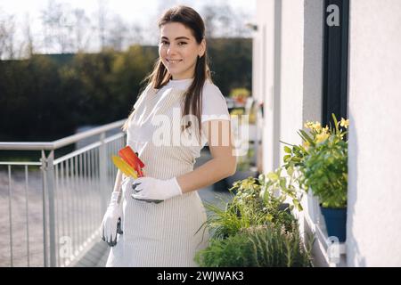 Junge attraktive Frau mit Gartengeräten steht auf dem Balkon und bereitet sich auf die Landung vor Stockfoto