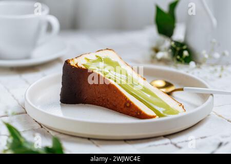 Beliebtes spanisches Dessert namens San Sebastian Käsekuchen. baskischer Käsekuchen mit verbranntem Käse. Ein Stück Kuchen auf weißem Hintergrund mit Pistazienglasur drauf. Stockfoto